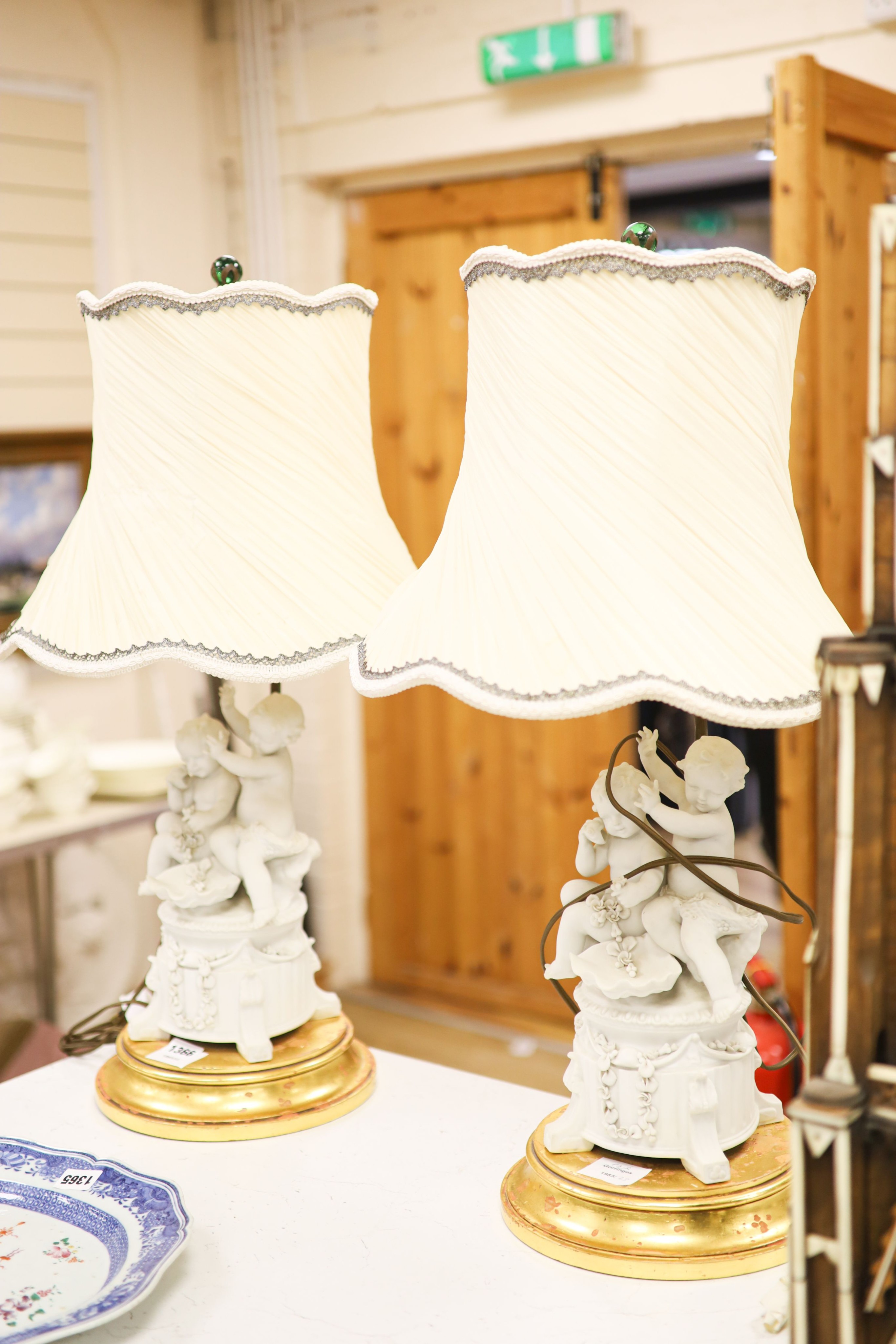 A pair of Sevres style biscuit porcelain groups of putti, fitted as a table lamps with shades 69cm total height incl shades